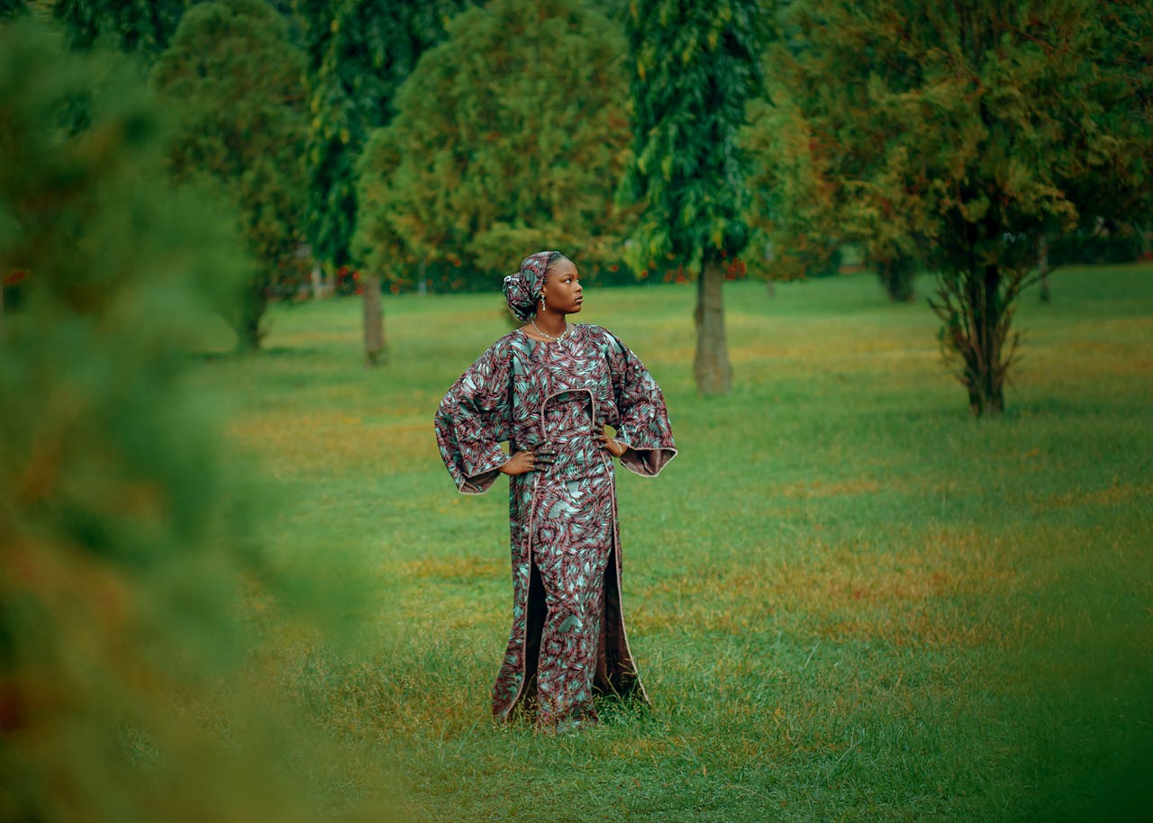 mobile-01 Woman in traditional African attire posing confidently in a lush green park.